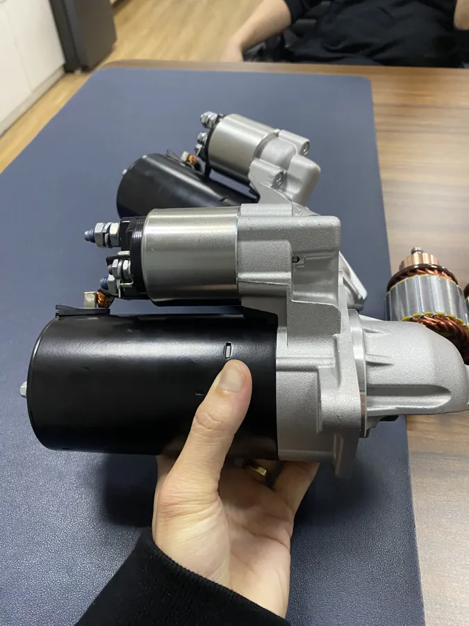 A hand holding a starter assembly with its housing, solenoid and drive end visible