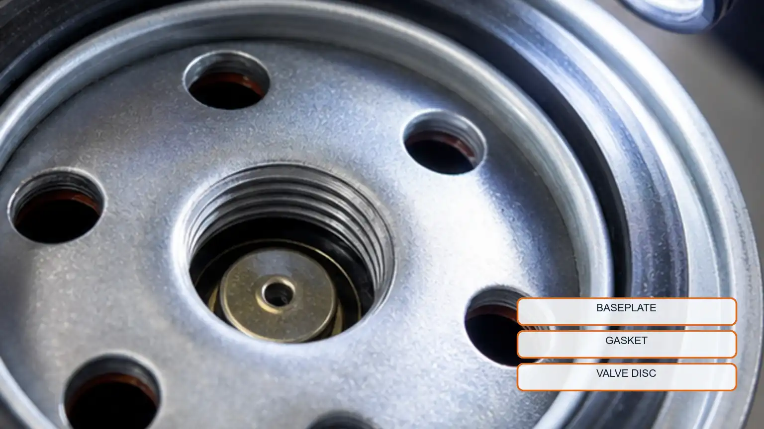 Macro inspection of a spin-on filter baseplate, gasket, inlet holes, center thread, and valve disc under a flashlight.