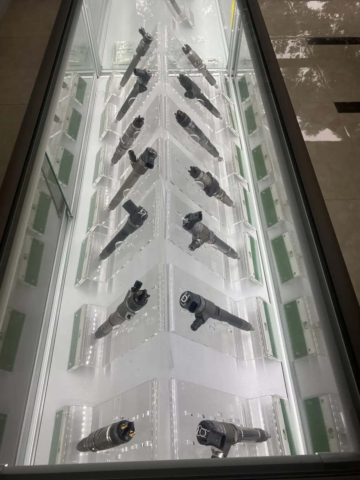 Different diesel injector samples arranged on acrylic stands in a glass display cabinet.